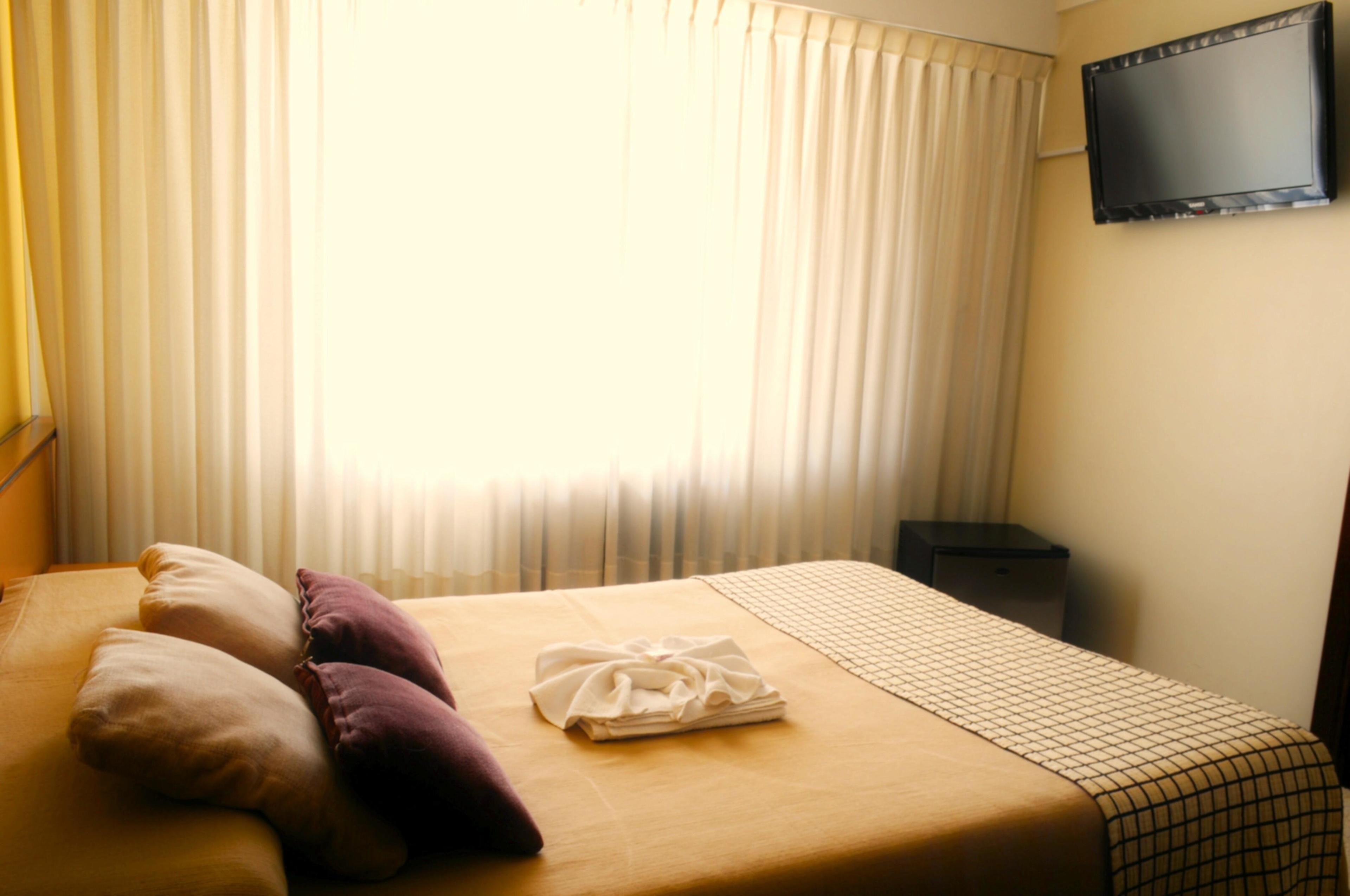 A hotel room with a bed, pillows, a folded towel, a TV on the wall, and a nightstand.