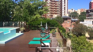 A rooftop pool area with lounge chairs and umbrellas, surrounded by greenery and residential buildings. - Don Carlos Hotel (Villa Gesell)