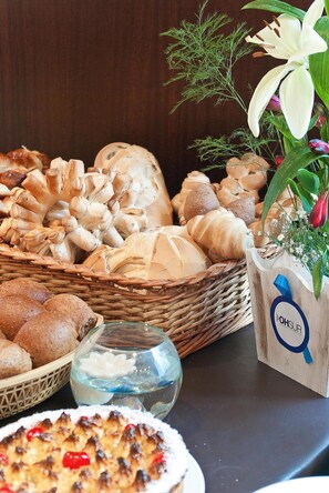 A variety of breads and pastries on a table, a glass of water, and a wooden planter with flowers. - Don Carlos Hotel (Villa Gesell)