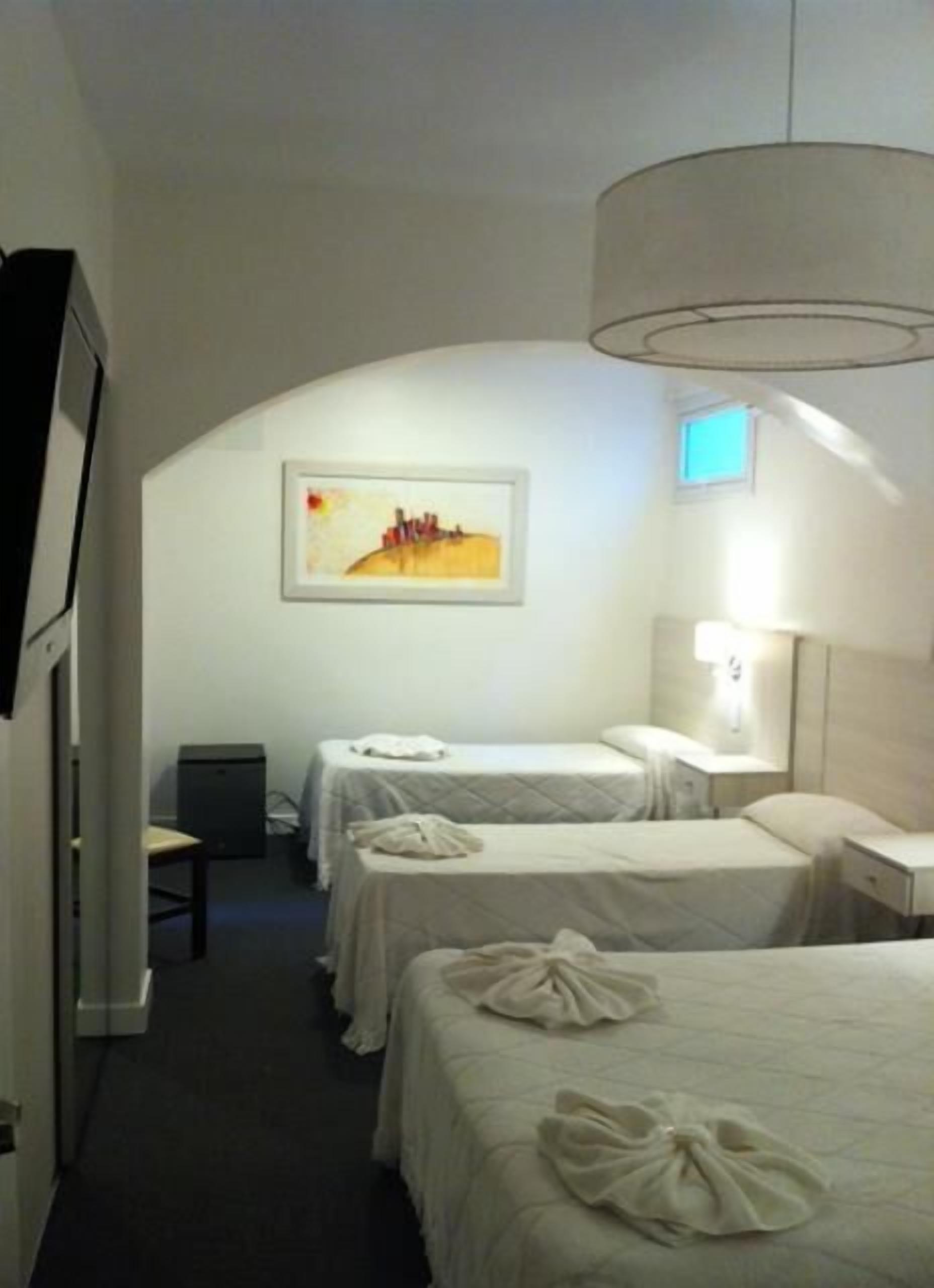A hotel room with two beds, a desk, a chair, a painting on the wall, and a ceiling light.