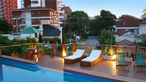 A rooftop pool area with lounge chairs and a table, surrounded by greenery and buildings. - Don Carlos Hotel (Villa Gesell)