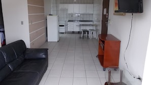 A compact living space with a kitchenette, a black leather sofa, and a TV mounted on the wall. - Rota do Pantanal Hotel (Presidente Prudente)
