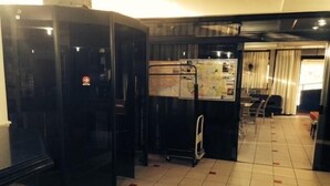 A hotel lobby with a tiled floor, a refrigerator, a cart, and a dining area in the background. - Rota do Pantanal Hotel (Presidente Prudente)