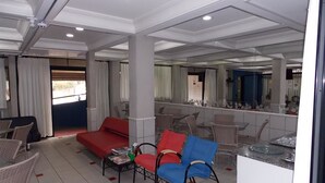 A hotel room with a red sofa, blue armchair, wicker chairs, a small table with magazines, and a large mirror reflecting the room. - Rota do Pantanal Hotel (Presidente Prudente)