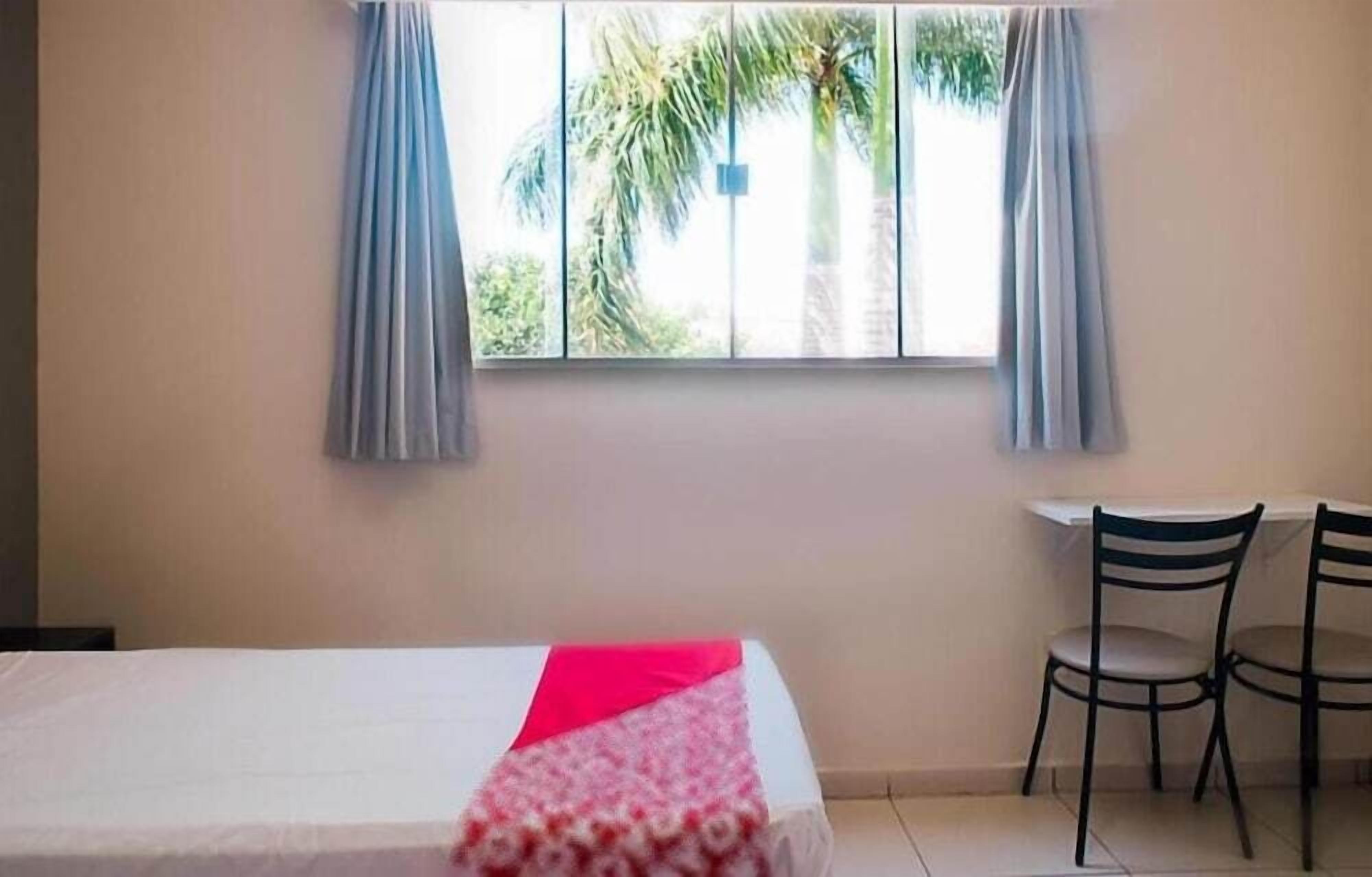 Quarto com uma cama, duas cadeiras e uma janela com cortinas.
