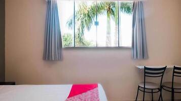 Quarto com uma cama, duas cadeiras e uma janela com cortinas.