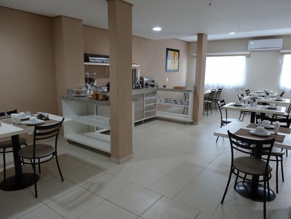 Un comedor moderno con varias mesas y sillas, una estación de buffet y una zona de cocina.