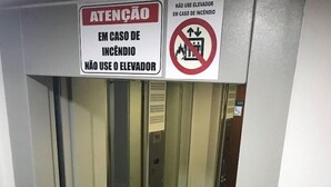 An elevator interior with glass doors, a sign indicating not to use the elevator in case of fire, and a carpeted floor. - Cerrado Hotel (Campo Grande)