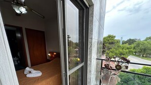 A hotel room with a bed, a nightstand, a lamp, and a view of greenery outside. - Hotel Sun Shine (San Clemente)