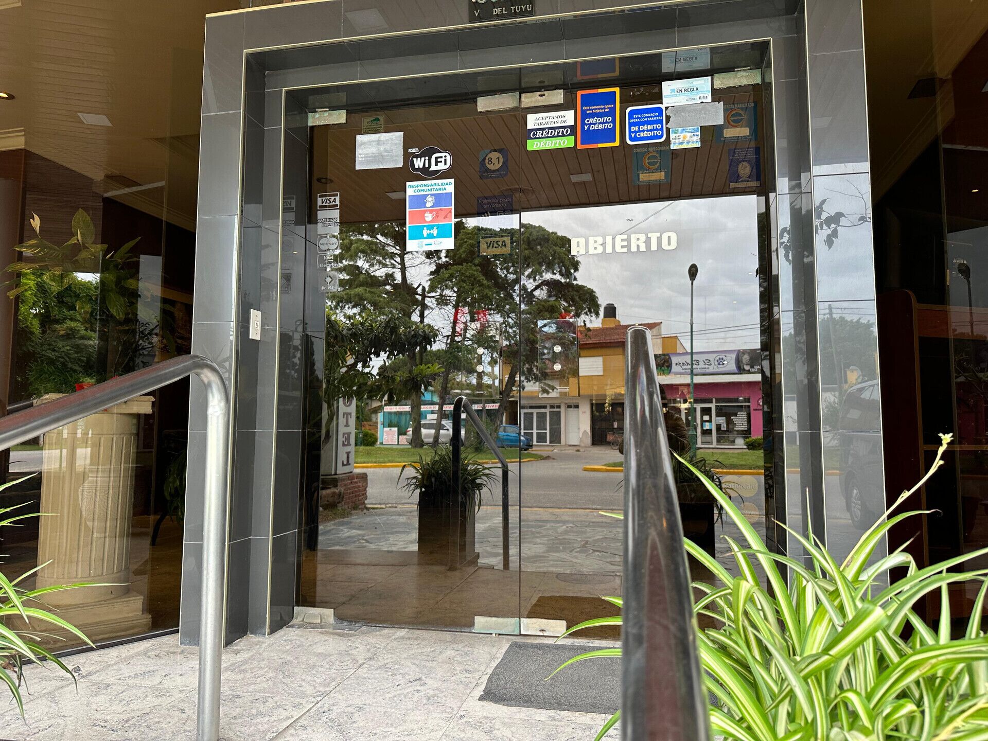 A hotel entrance with a glass door, a staircase, and various signs indicating amenities like Wi-Fi, credit/debit card acceptance, and community responsibility.