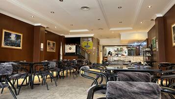 Un amplio vestíbulo de hotel con varias zonas de estar, un bar central y una escalera que sube a un piso superior.