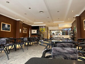 A spacious hotel lobby with multiple seating areas, a central bar, and a staircase leading to an upper floor.