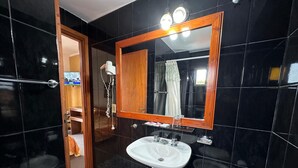 A bathroom with a white sink, a wooden-framed mirror, and black tiled walls. - Hotel Sun Shine (San Clemente)