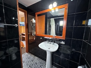 A bathroom with a white sink, a wooden-framed mirror, and black tiled walls. - Hotel Sun Shine (San Clemente)