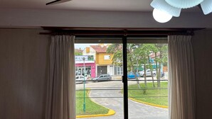 A room with a ceiling fan, a view of the street outside through a glass door, and a yellow curb visible in the reflection. - Hotel Sun Shine (San Clemente)