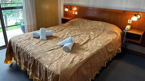 A hotel room with a large bed, two bedside lamps, a telephone, and a window with a view of greenery. - Hotel Sun Shine (San Clemente)