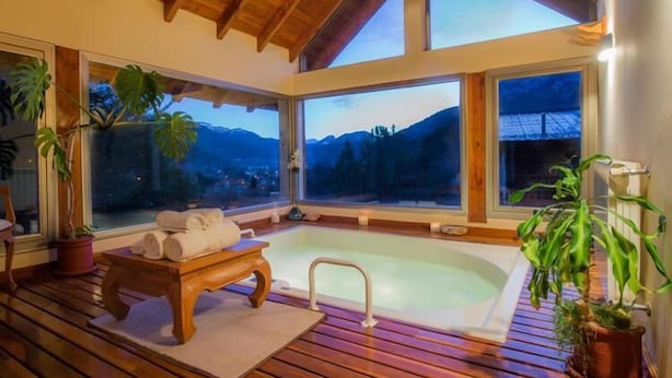 A spa area with a hot tub, wooden flooring, and large windows offering mountain views. - Cabañas y Apart Antuen (San Martin de los Andes)