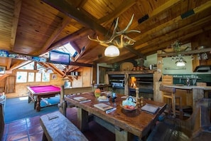 A rustic lodge interior with a pool table, wooden dining table, and a television.