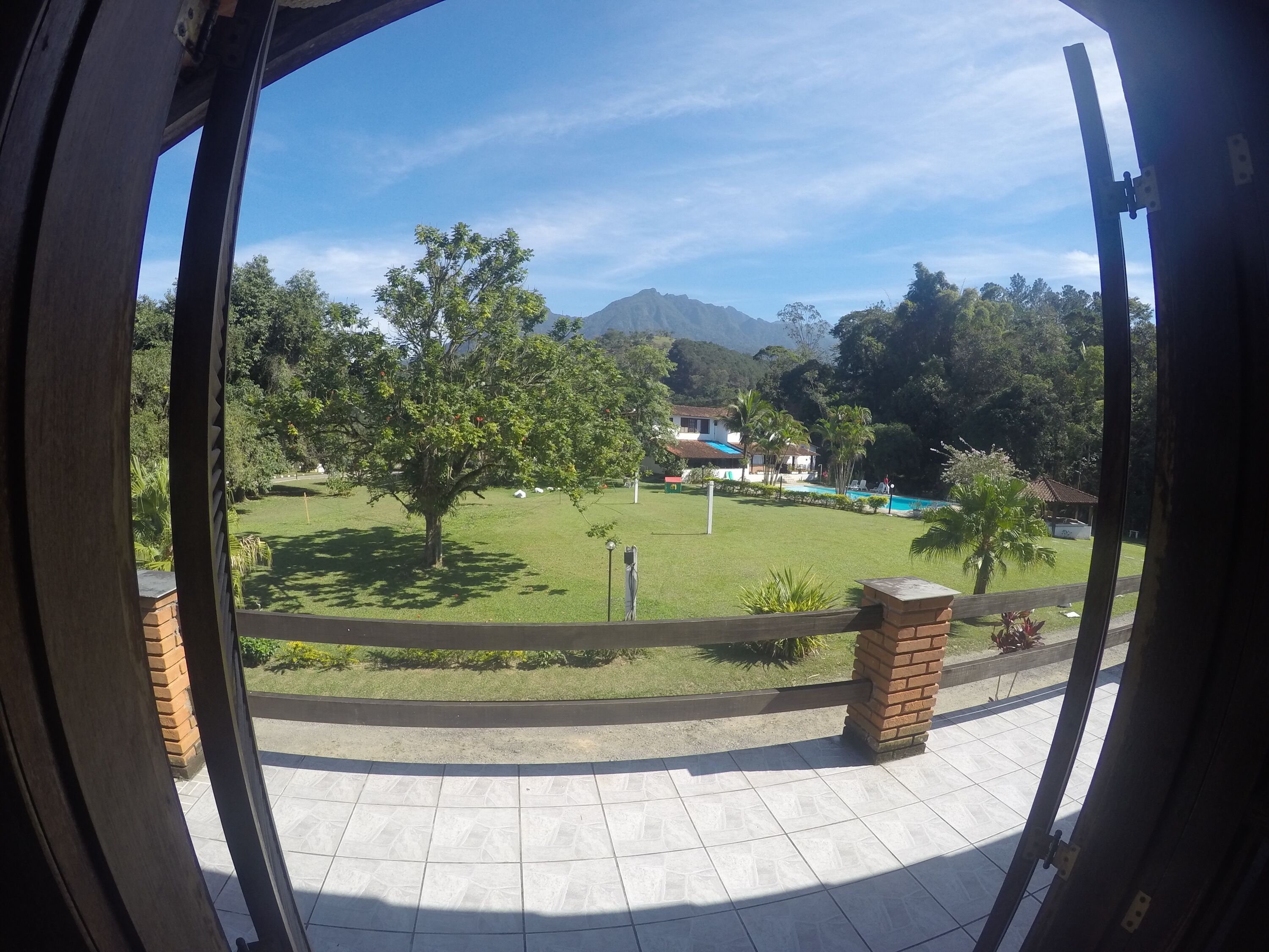 Vista a través de un umbral de un patio con piscina, árboles y una montaña al fondo.