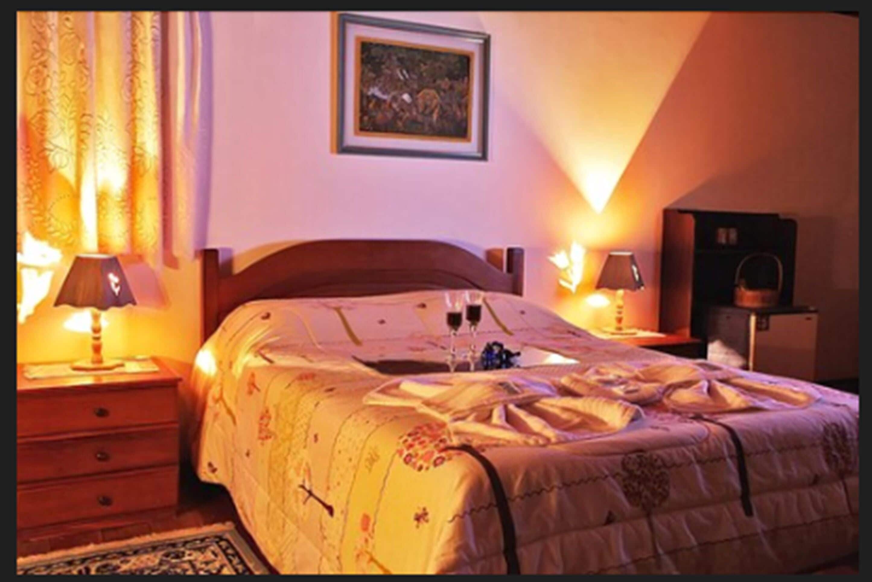 Une chambre à coucher avec un lit, deux tables de chevet avec des lampes, une commode, un tableau encadré au mur et un petit meuble.