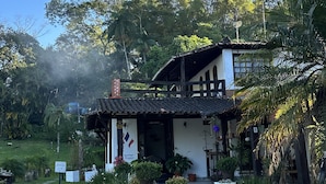Un bâtiment à deux étages, doté d’un toit en tuiles, entouré d’une végétation luxuriante et de palmiers.