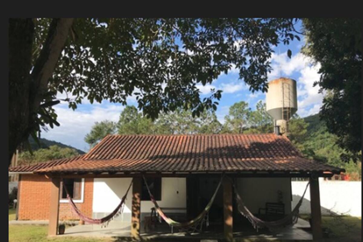 Un petit bâtiment en briques, avec un toit en tuiles, un hamac et un château d’eau en arrière-plan.