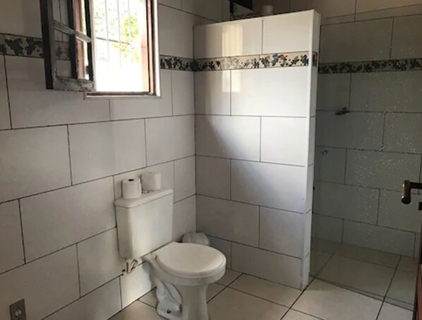 Un baño con azulejos blancos, un inodoro y una cabina de ducha.