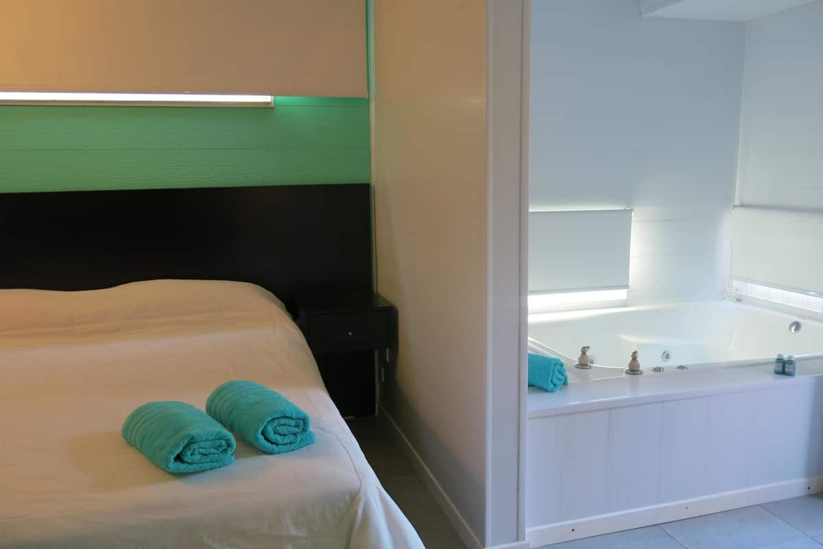 A hotel room with a bed, a nightstand, a white bathtub, and a window.