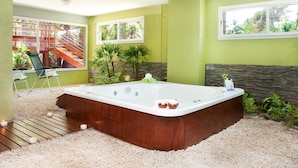 A spa room with a large bathtub, a wooden deck, and a view of a staircase and greenery outside. - Oasis Apart Hotel (Mar Azul)