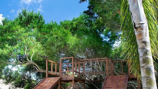 A wooden deck with a slide, surrounded by greenery and a clear sky. - Oasis Apart Hotel (Mar Azul)