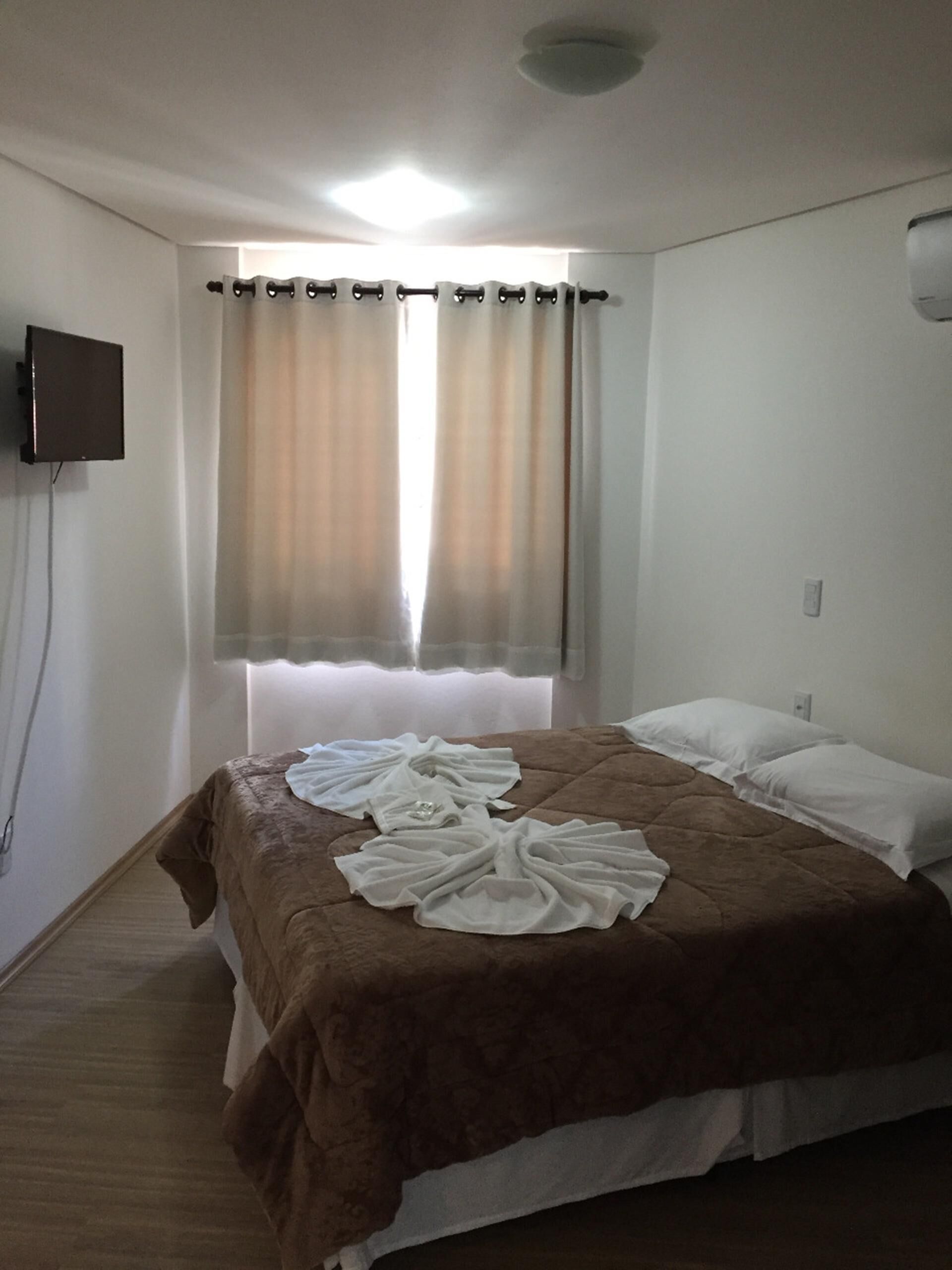A hotel room with a bed, curtains, a flat-screen TV, and a ceiling light.