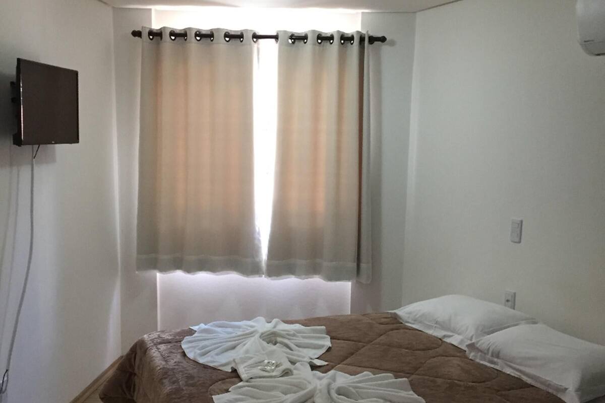 A hotel room with a bed, curtains, a flat-screen TV, and a ceiling light.