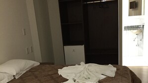 A hotel room with a bed, a wardrobe, a small desk, and a bathroom visible through an open door.