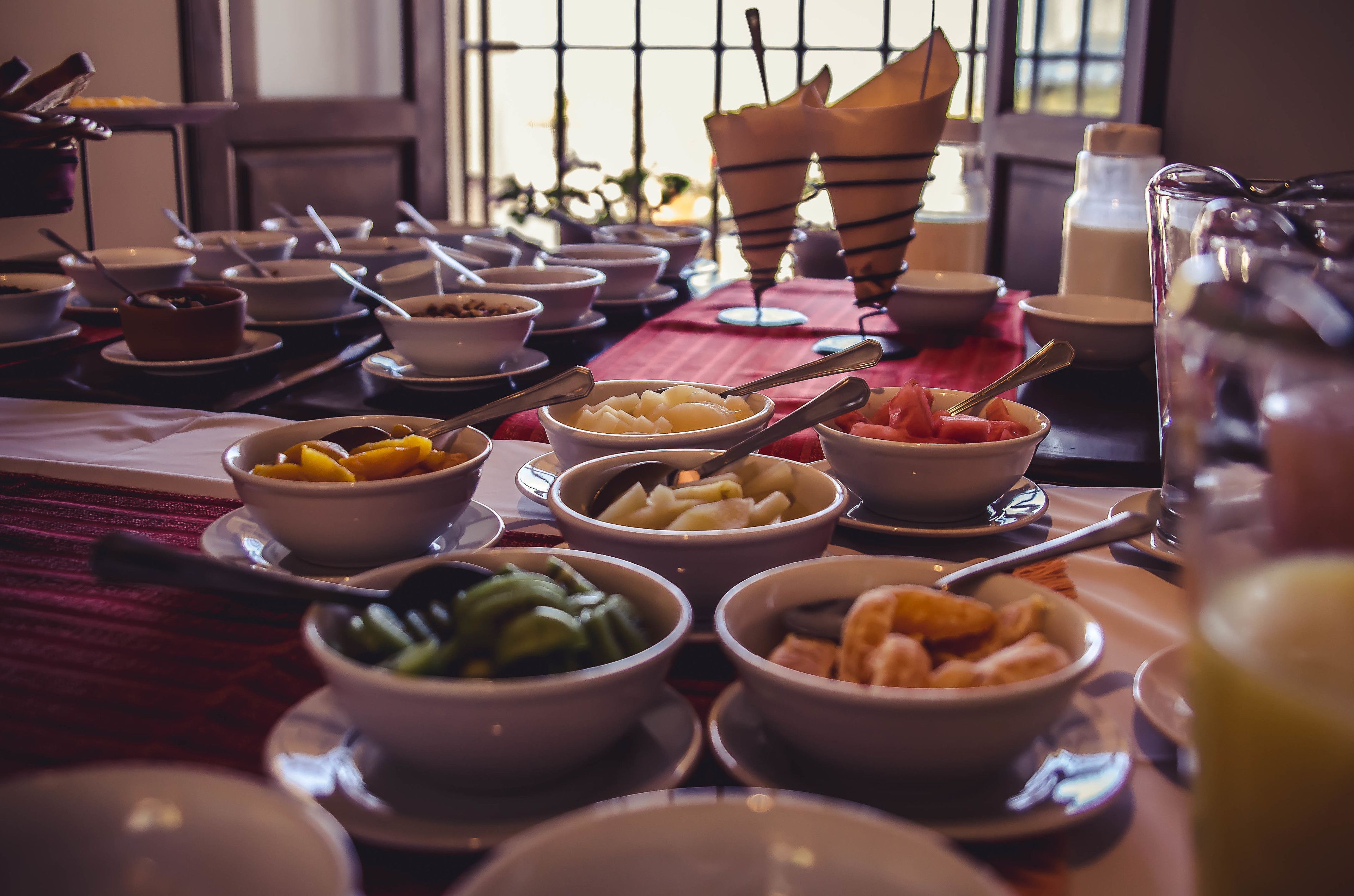 Uma mesa posta com várias tigelas de comida, incluindo frutas e legumes, e um jarro de vidro.