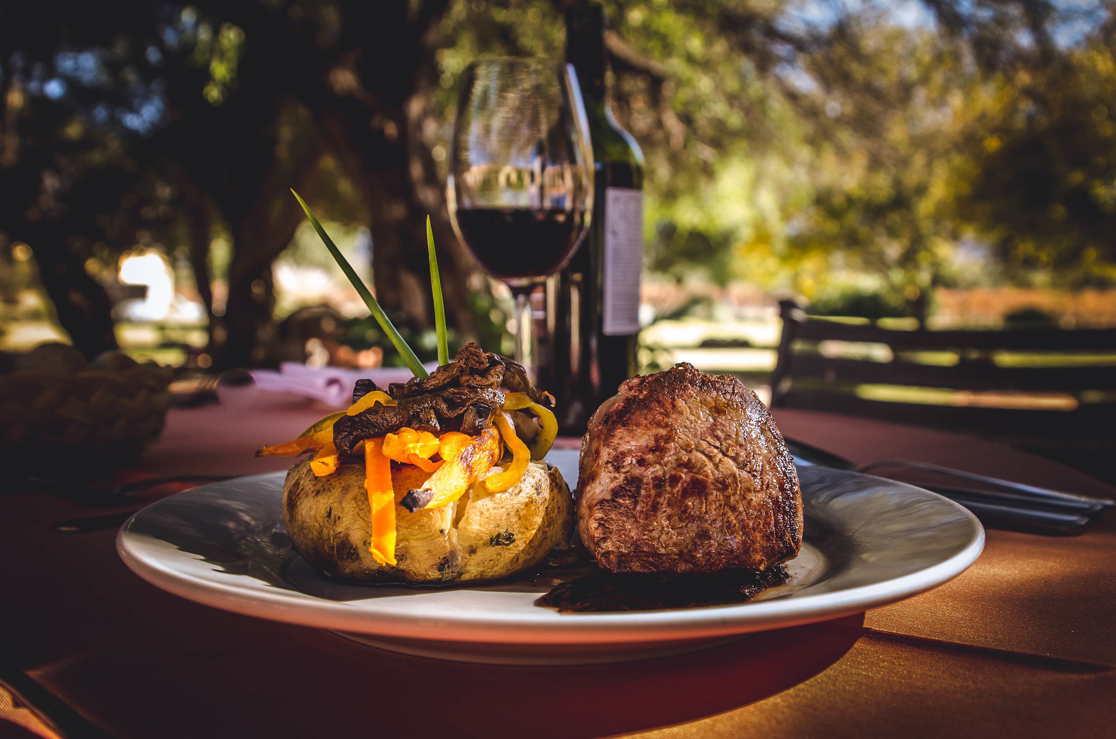 A plate with a steak and roasted vegetables on a table outdoors.
