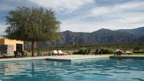 Un espace piscine avec des chaises longues et un arbre, le tout entouré de montagnes.
