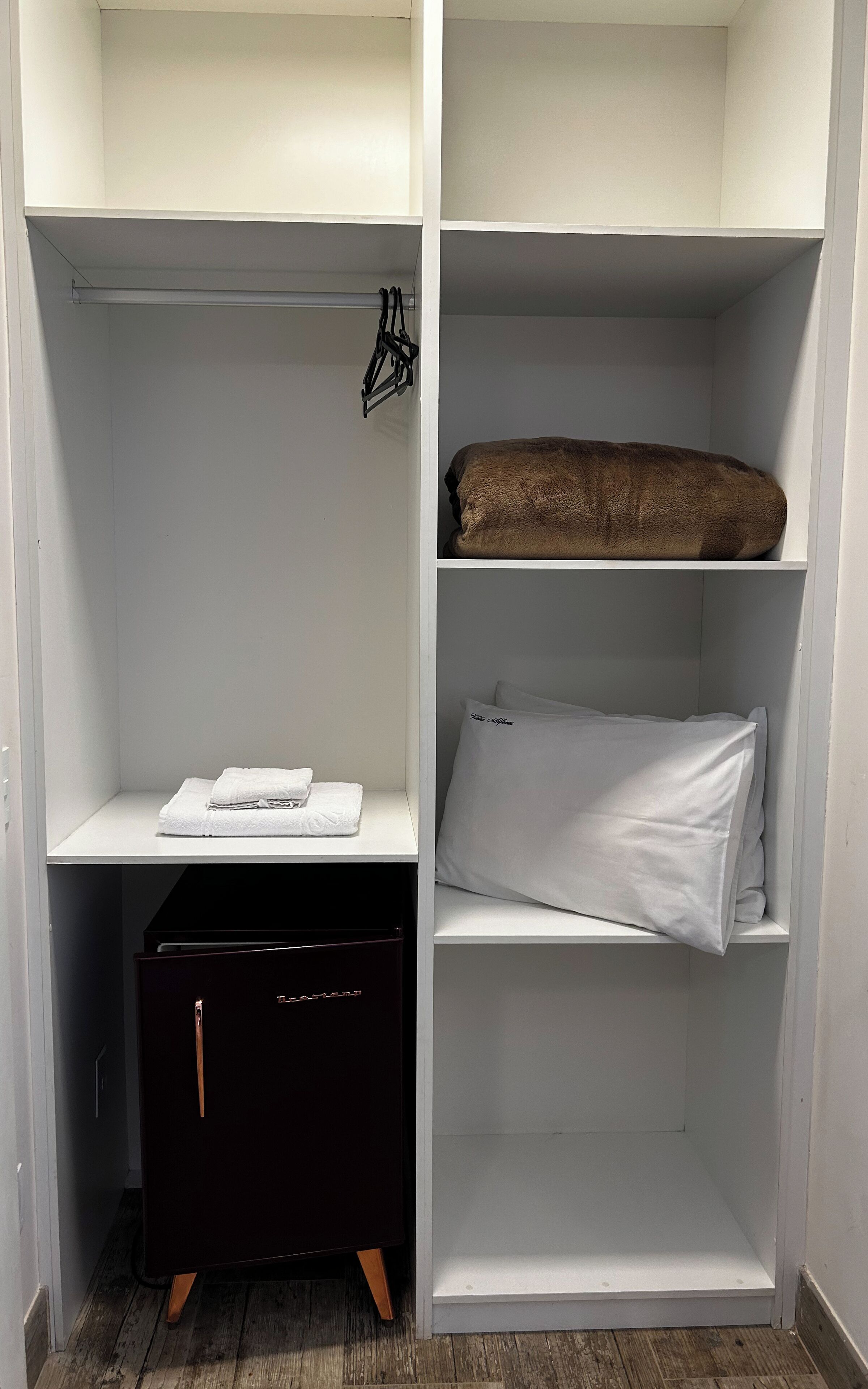 Ein begehbarer Kleiderschrank mit offenen Regalen, einer Kleiderstange und einer schwarzen Aufbewahrungsbox.