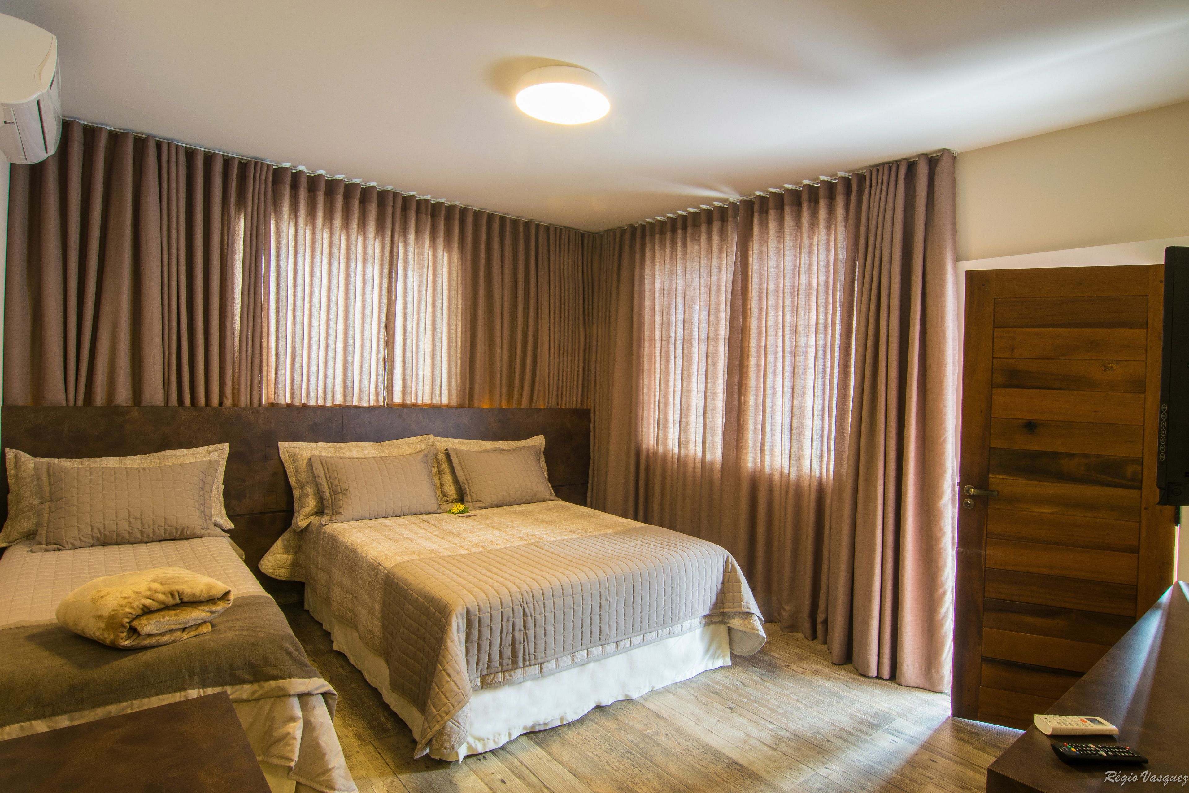 A hotel room with two beds, a wooden headboard, a wooden door, and a flat-screen TV on a wooden stand.