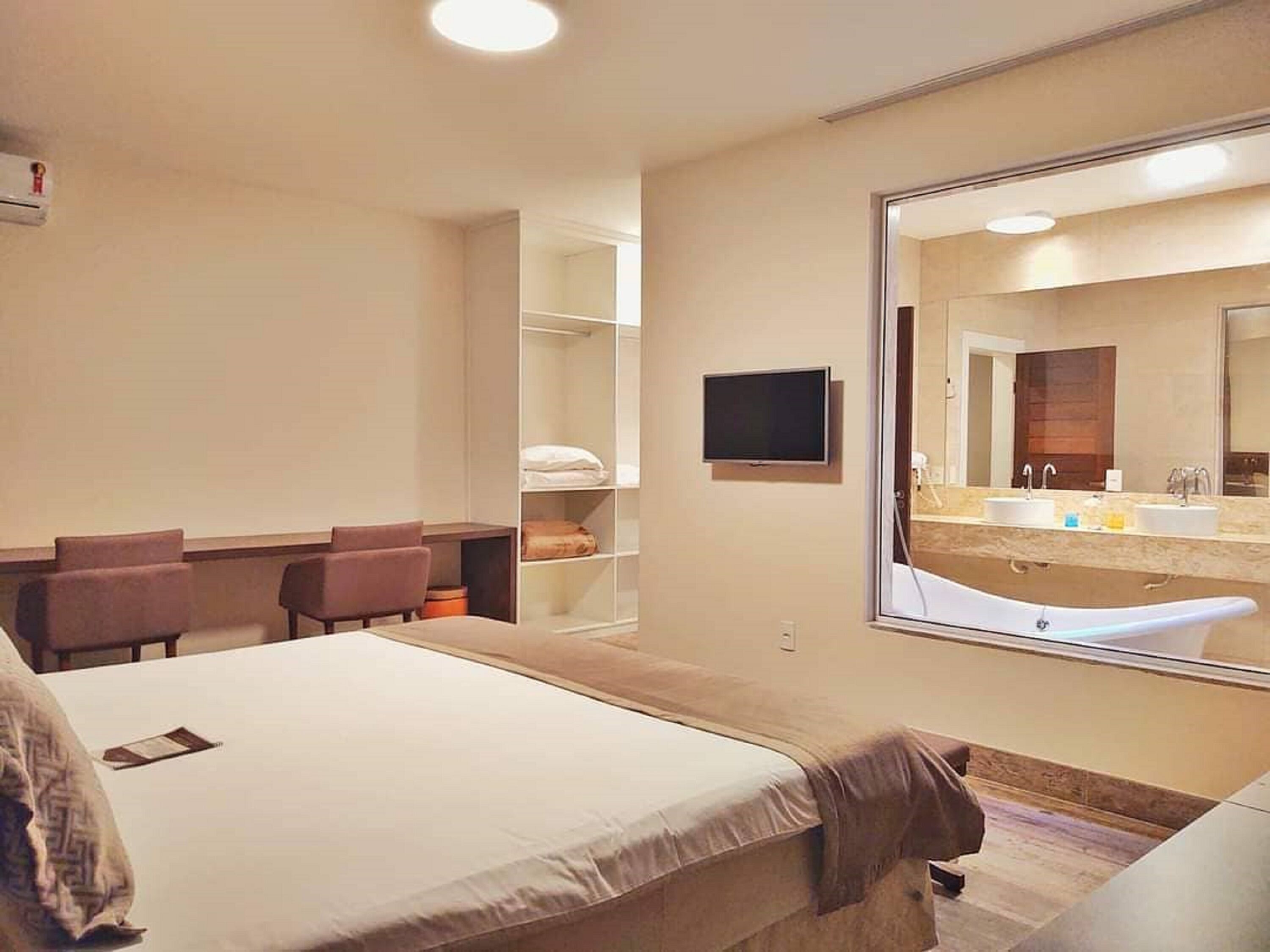 A hotel room with a large bed, a desk, a chair, a TV, and a bathroom with a bathtub and sink.