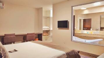 A hotel room with a large bed, a desk, a chair, a TV, and a bathroom with a bathtub and sink.