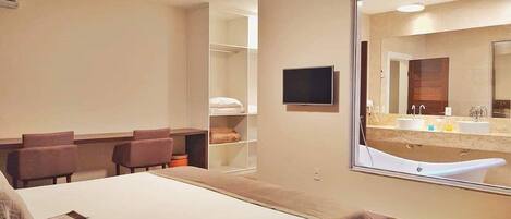 A hotel room with a large bed, a desk, a chair, a TV, and a bathroom with a bathtub and sink.
