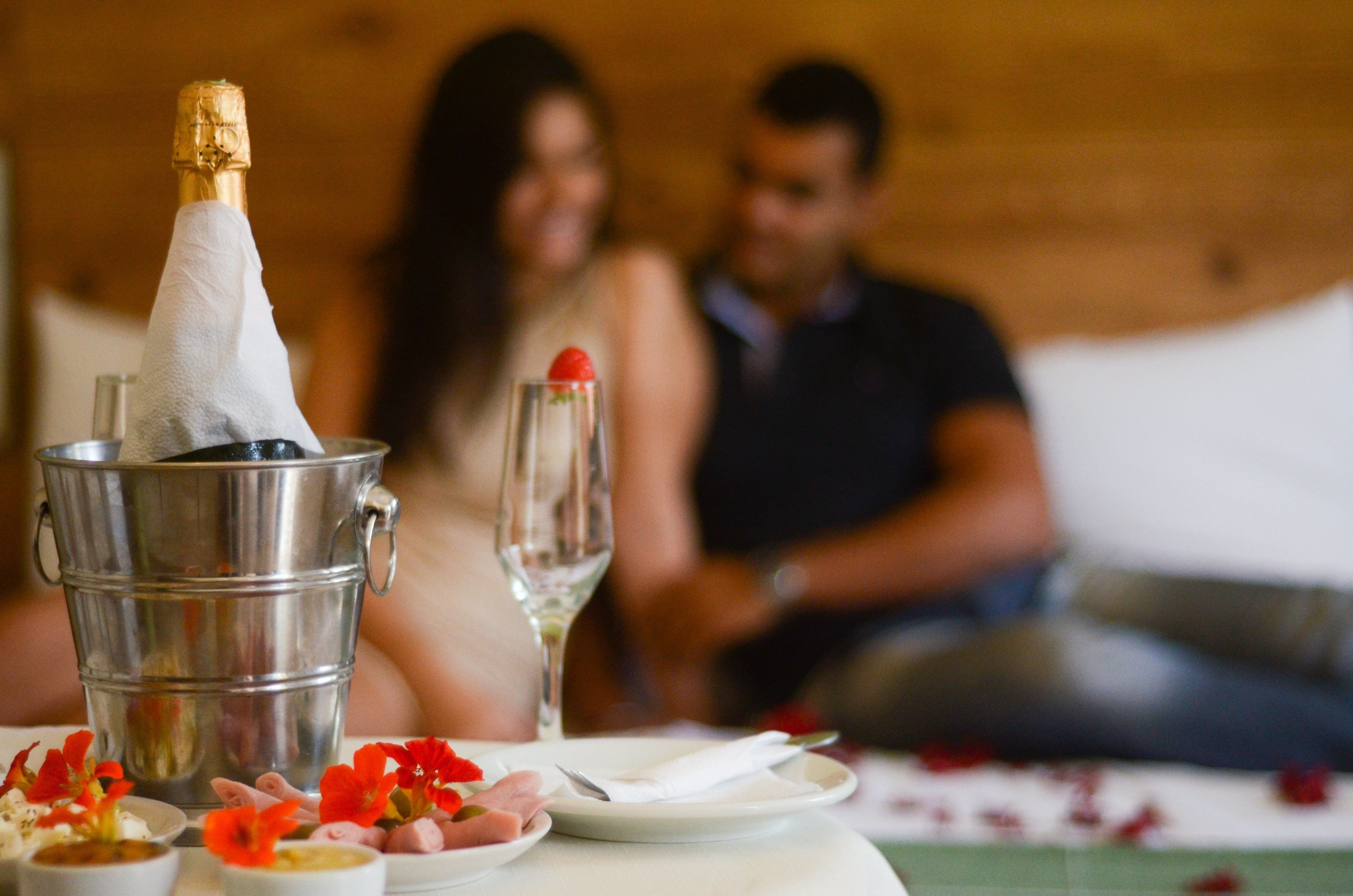 Una mesa de comedor con una botella de champán, una copa, y platos con comida y flores.