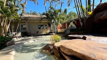 Un espace piscine avec une eau cristalline, entouré de palmiers et bordé d’un bâtiment doté d’un toit en tuiles.