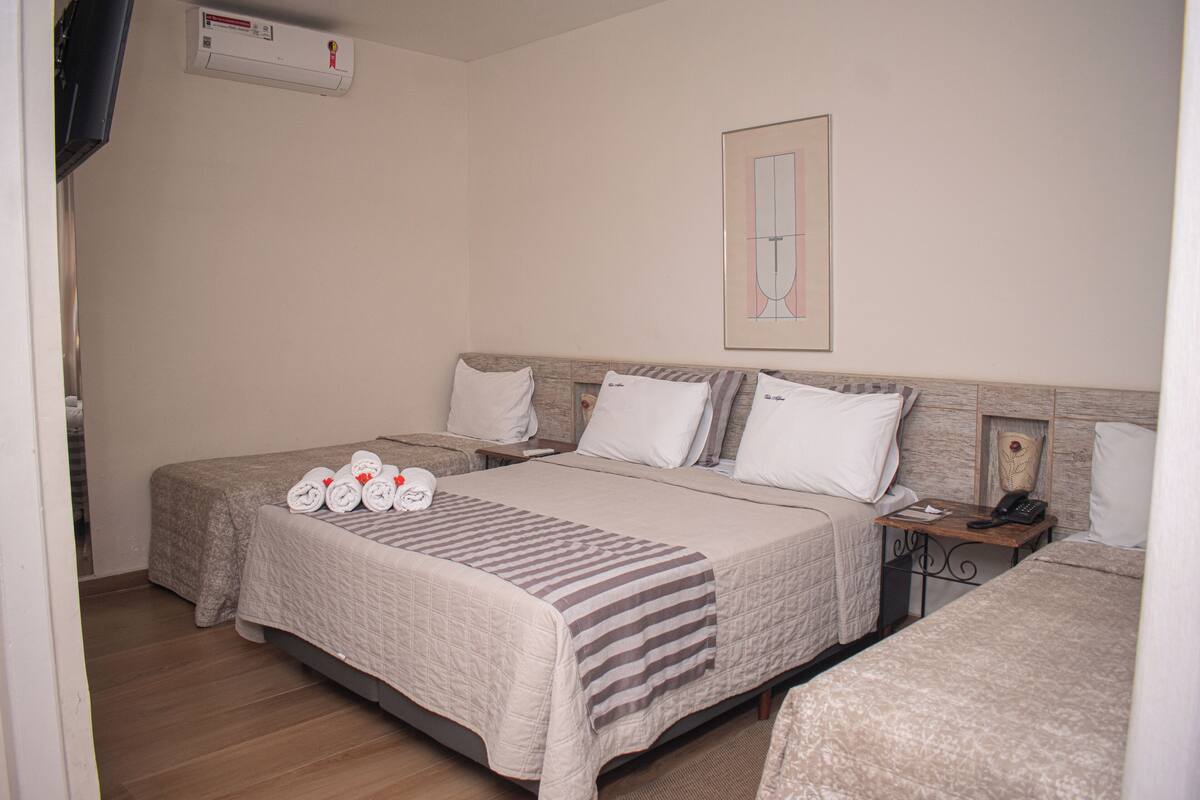 A hotel room with two beds, a bedside table with a phone, and a wall-mounted air conditioner.