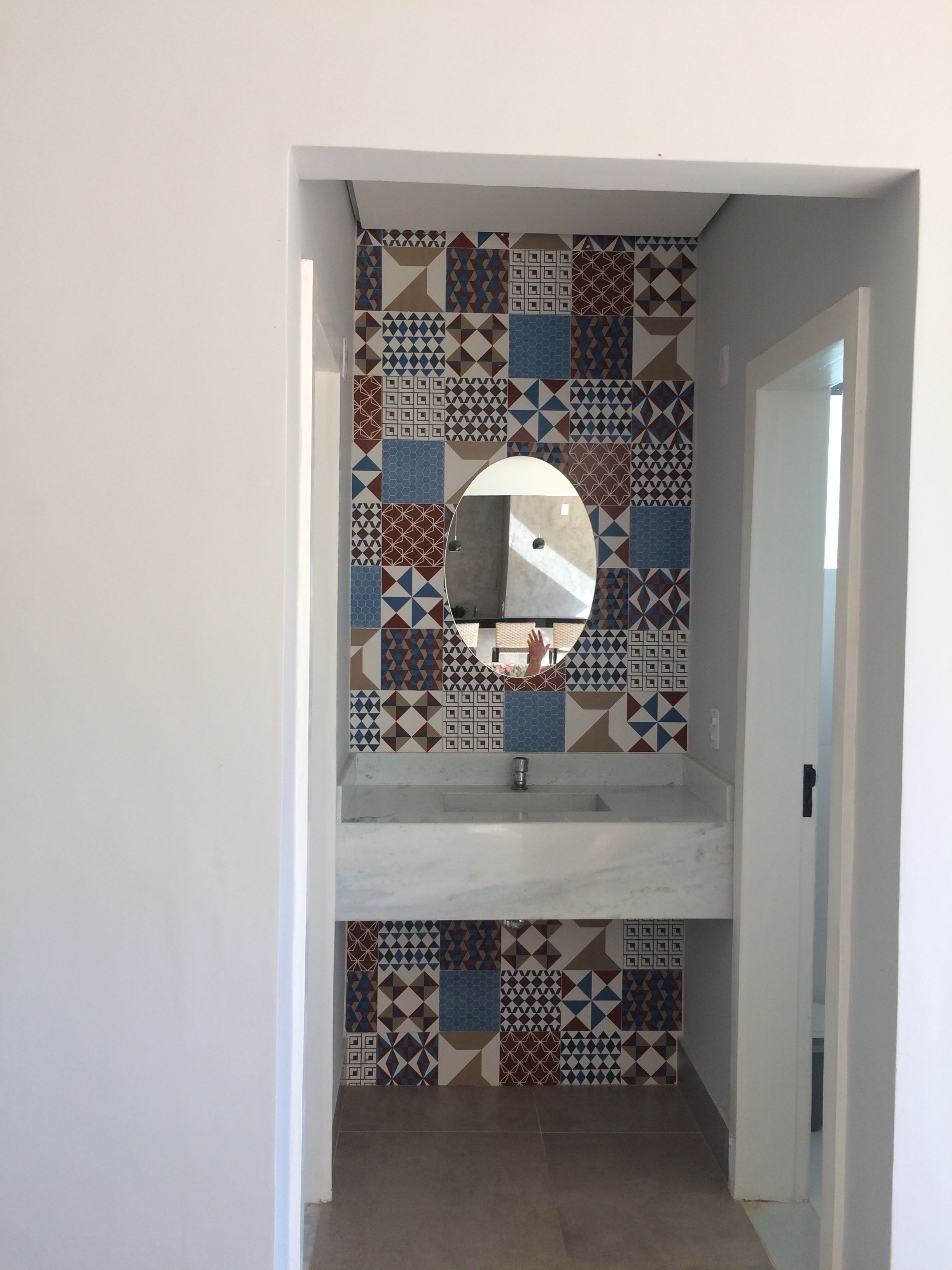 A bathroom with a tiled backsplash featuring geometric patterns and a round mirror above a sink.