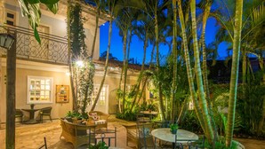 Un patio con mobiliario exterior, palmeras y un edificio con balcón.