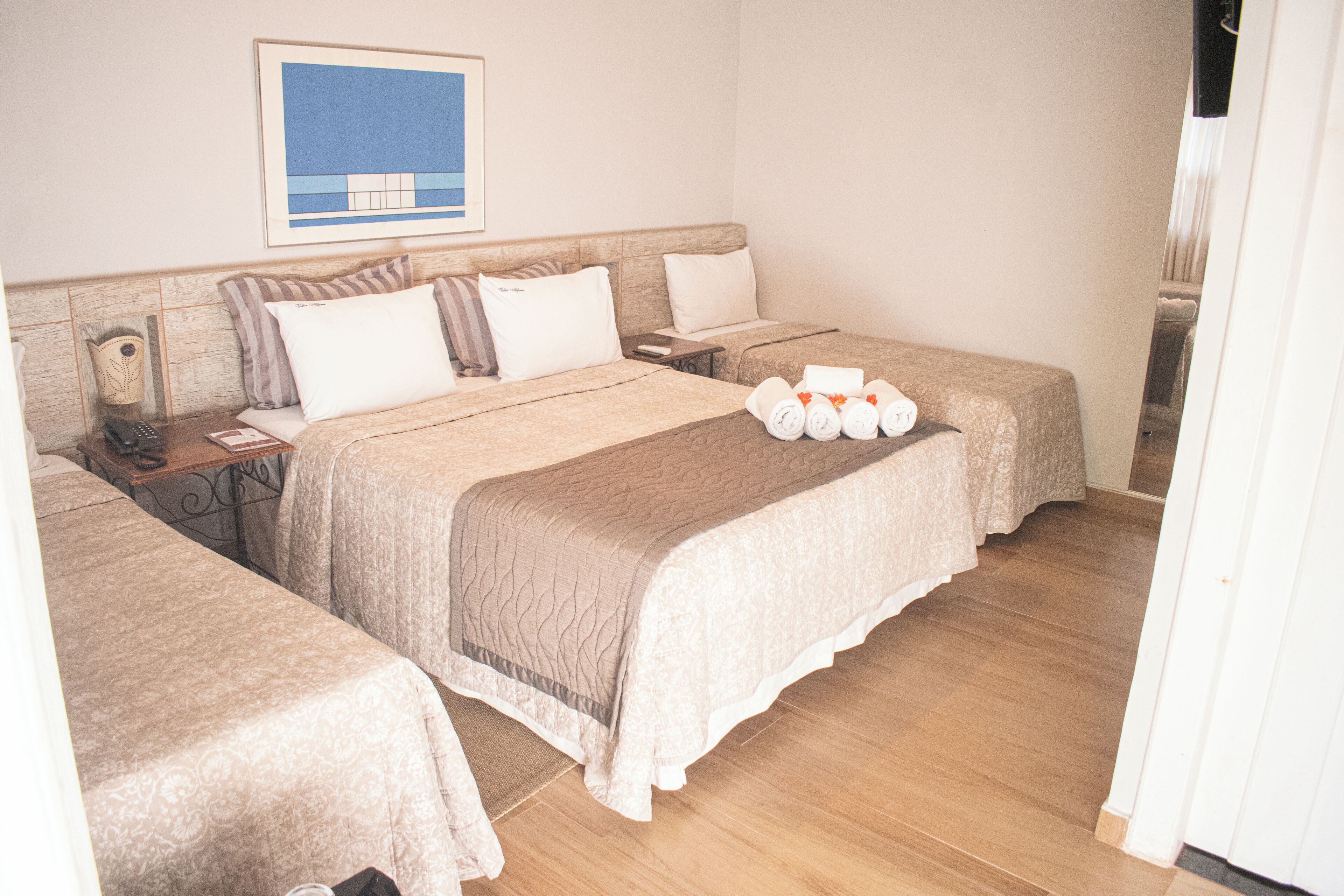 A hotel room with two beds, a nightstand, a framed picture on the wall, and a neatly made bed with towels.