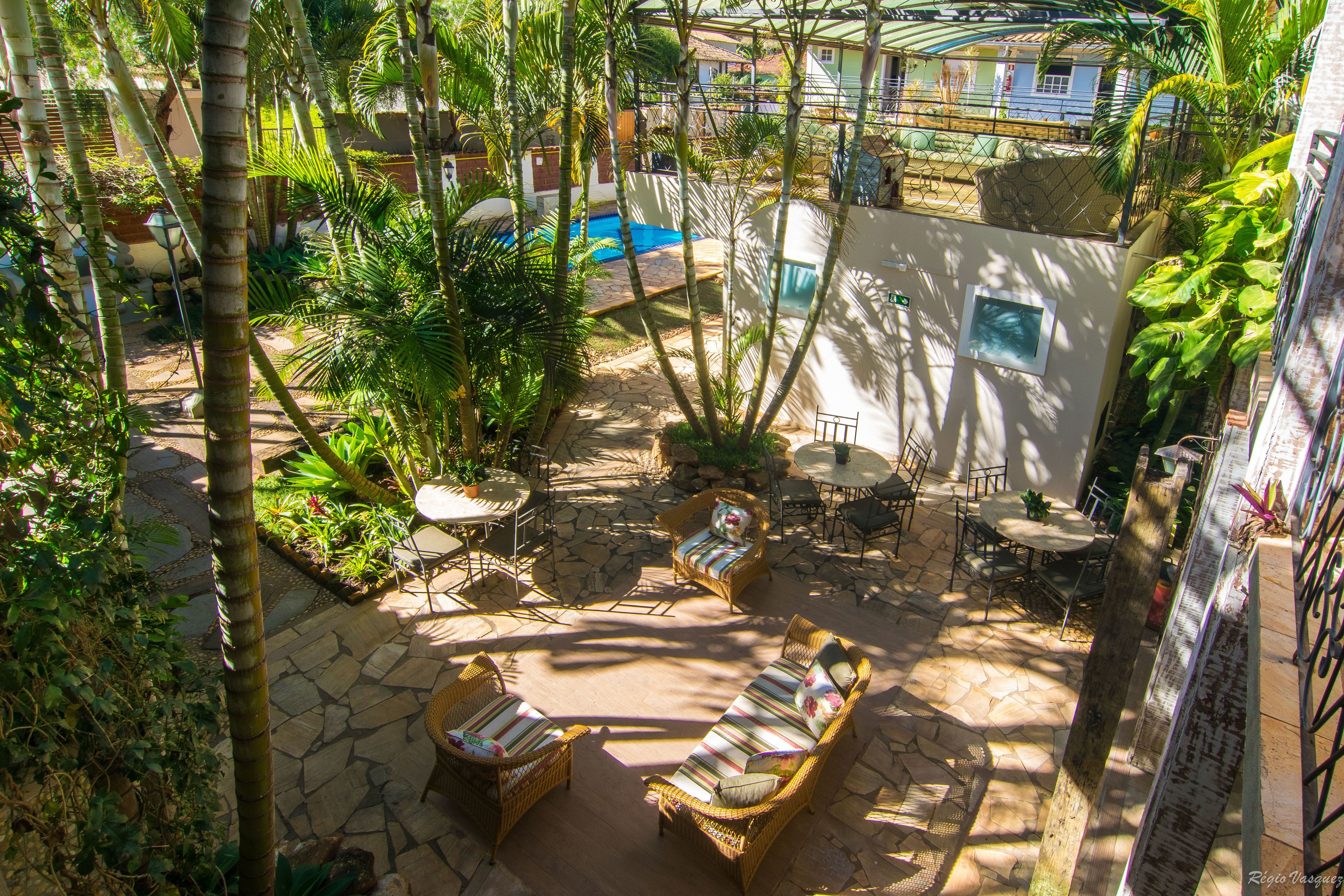 Un patio con mobiliario de mimbre, suelo de piedra y una piscina al fondo.
