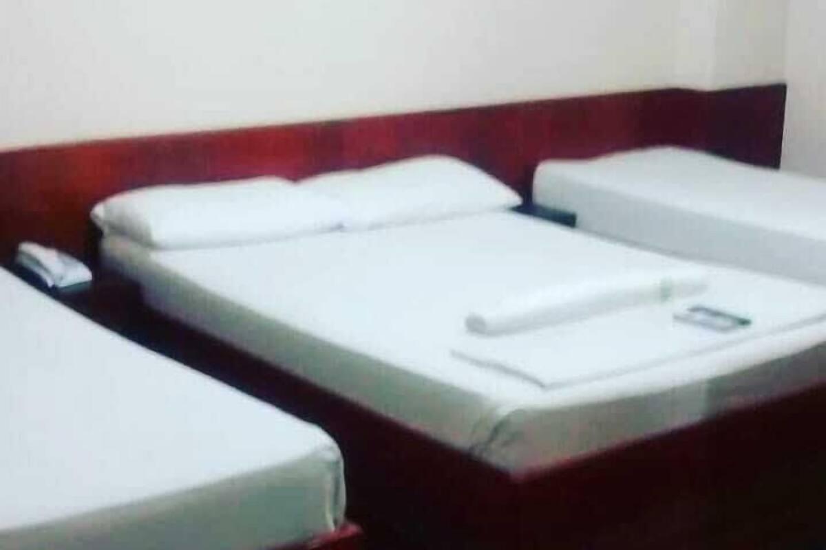 A hotel room with three single beds, each with a white mattress and matching pillows.