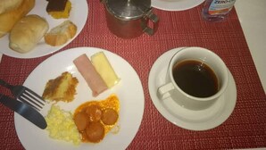 Una mesa de desayuno con platos de comida, una taza de café y una botella de salsa.